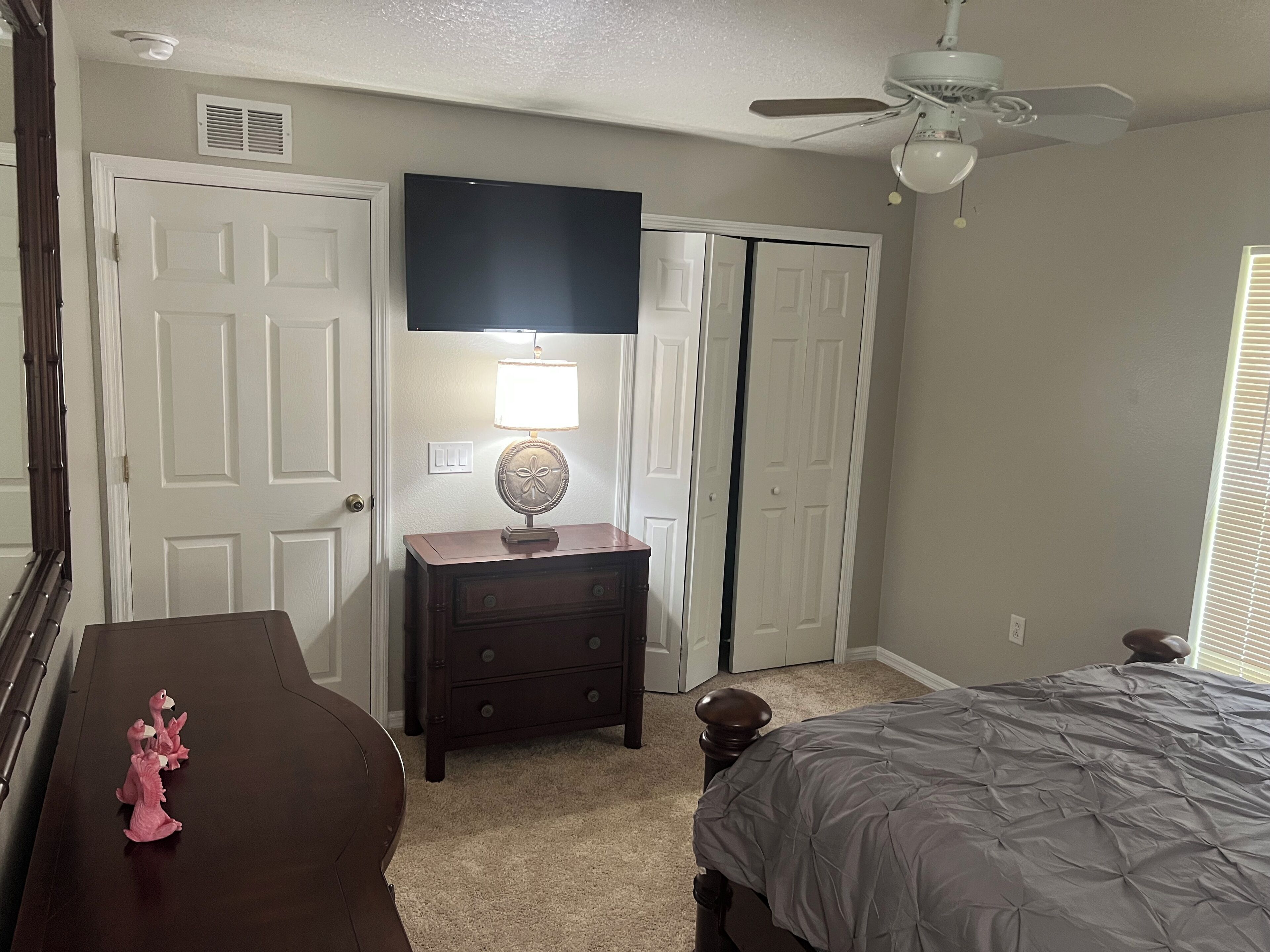 A bedroom with a bed, dresser, lamp, and a ceiling fan.