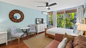 Un dormitorio con cama, escritorio, silla, televisor y ventana con vista a zonas verdes.
