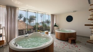 A room with two hot tubs, a large window with a view of palm trees, and a wooden floor. - 🌴 Luxury Beachfront Apartment in Mazatlan's Golden Zone - Pool & Oceanfront (Mazatlán)