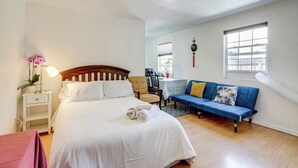 Une chambre à coucher avec un lit, un canapé bleu, une chaise en bois, une petite table et une fenêtre.