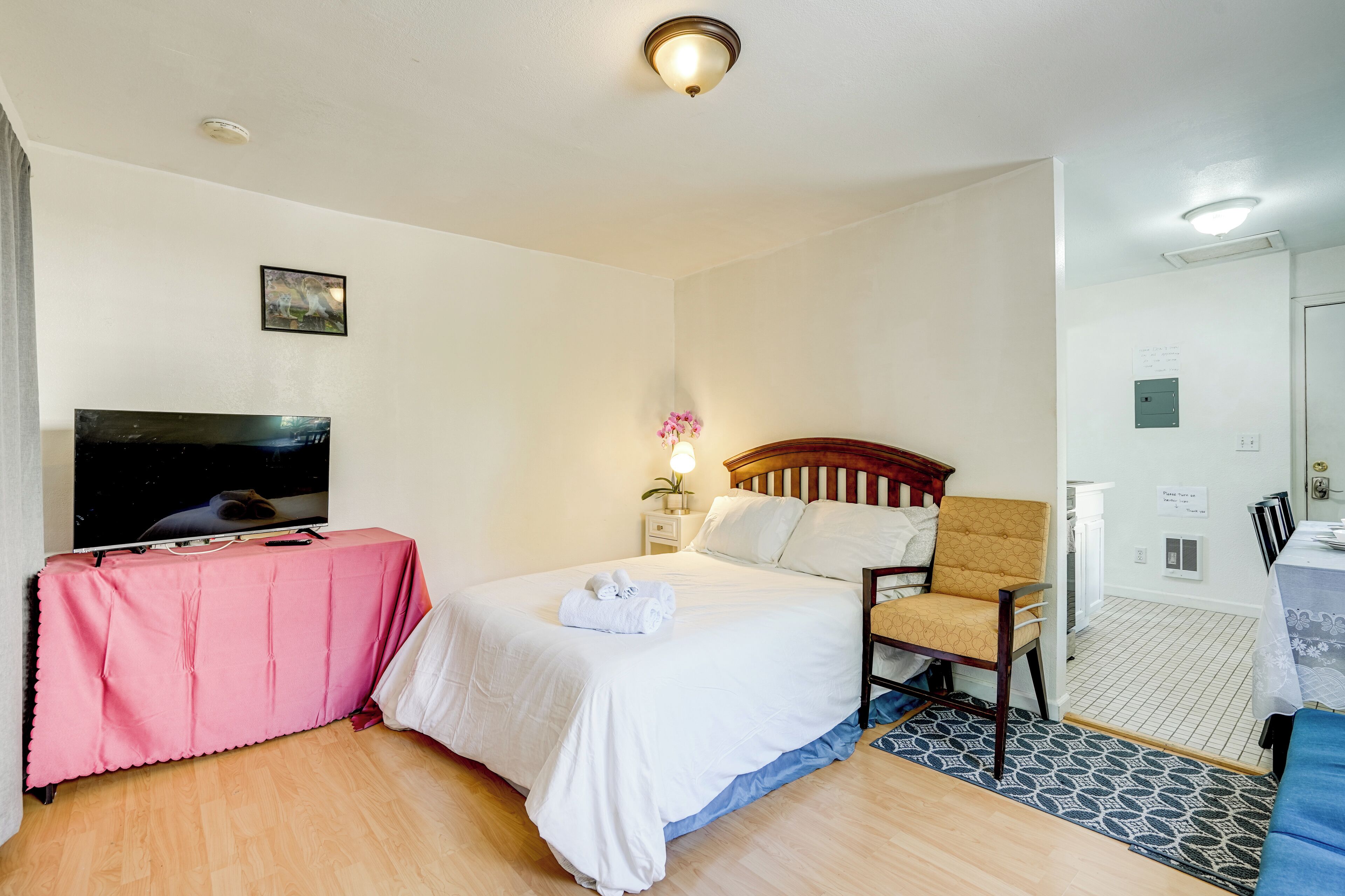Une chambre d’hôtel avec un lit, une télévision, une chaise et un bureau recouvert d’une nappe rose.
