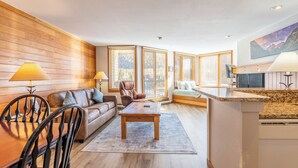 A modern living room with a wooden wall, a sofa, a coffee table, and a dining area with chairs. - Ls1489-0 (Keystone)