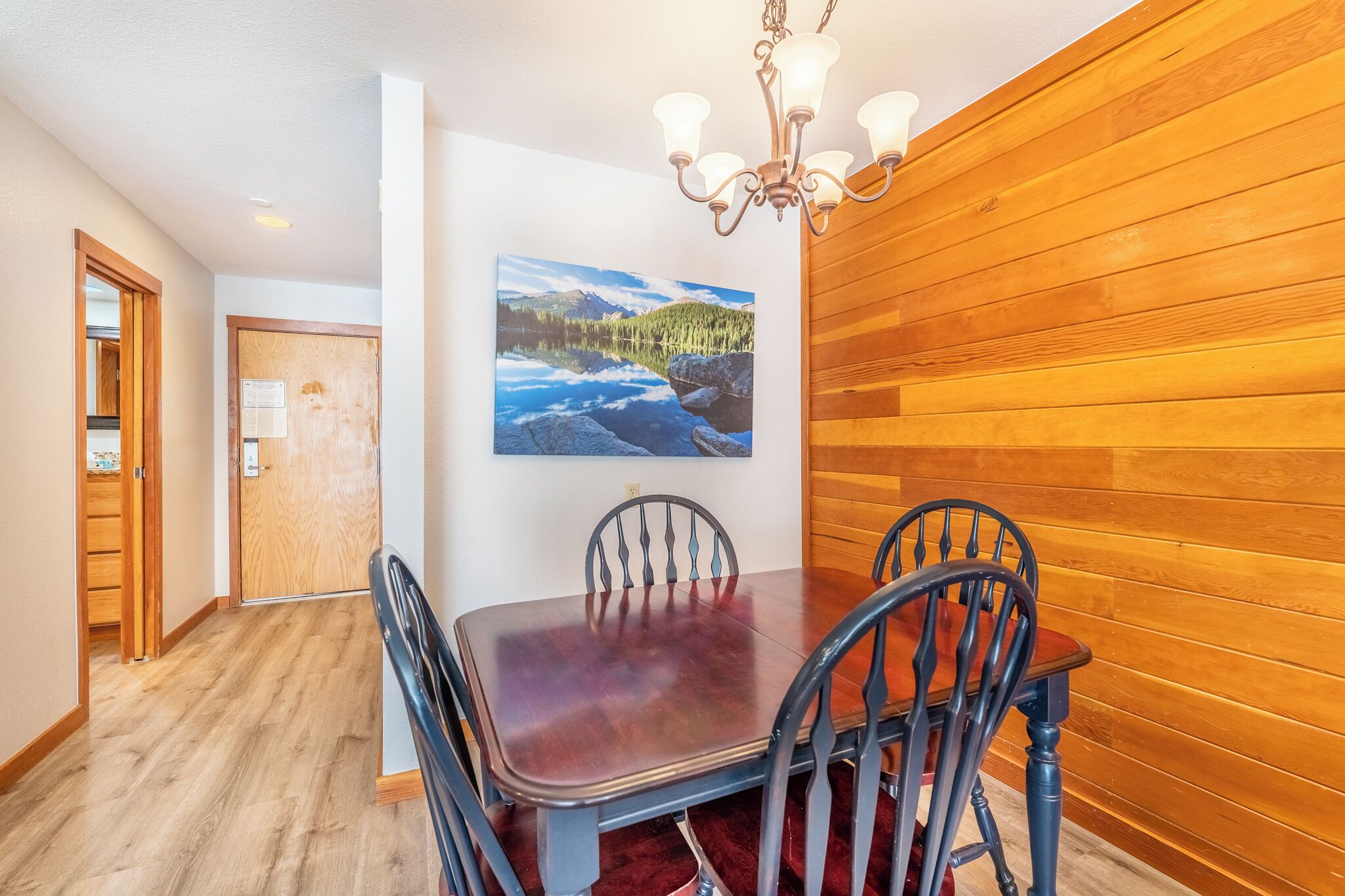 Un comedor con pared de madera, una araña y un cuadro de un lago.