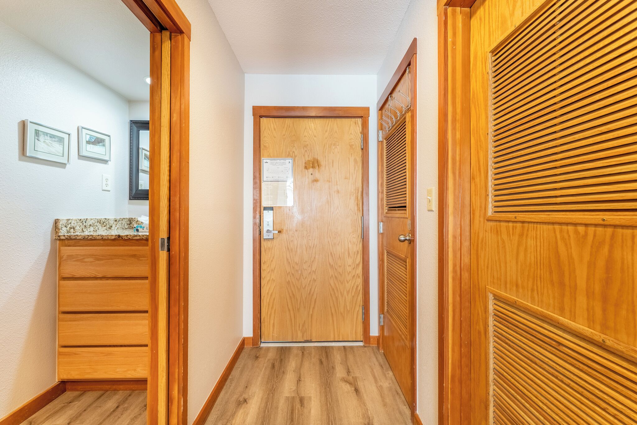 Un couloir avec des portes en bois, un meuble en bois et un miroir fixé au mur.