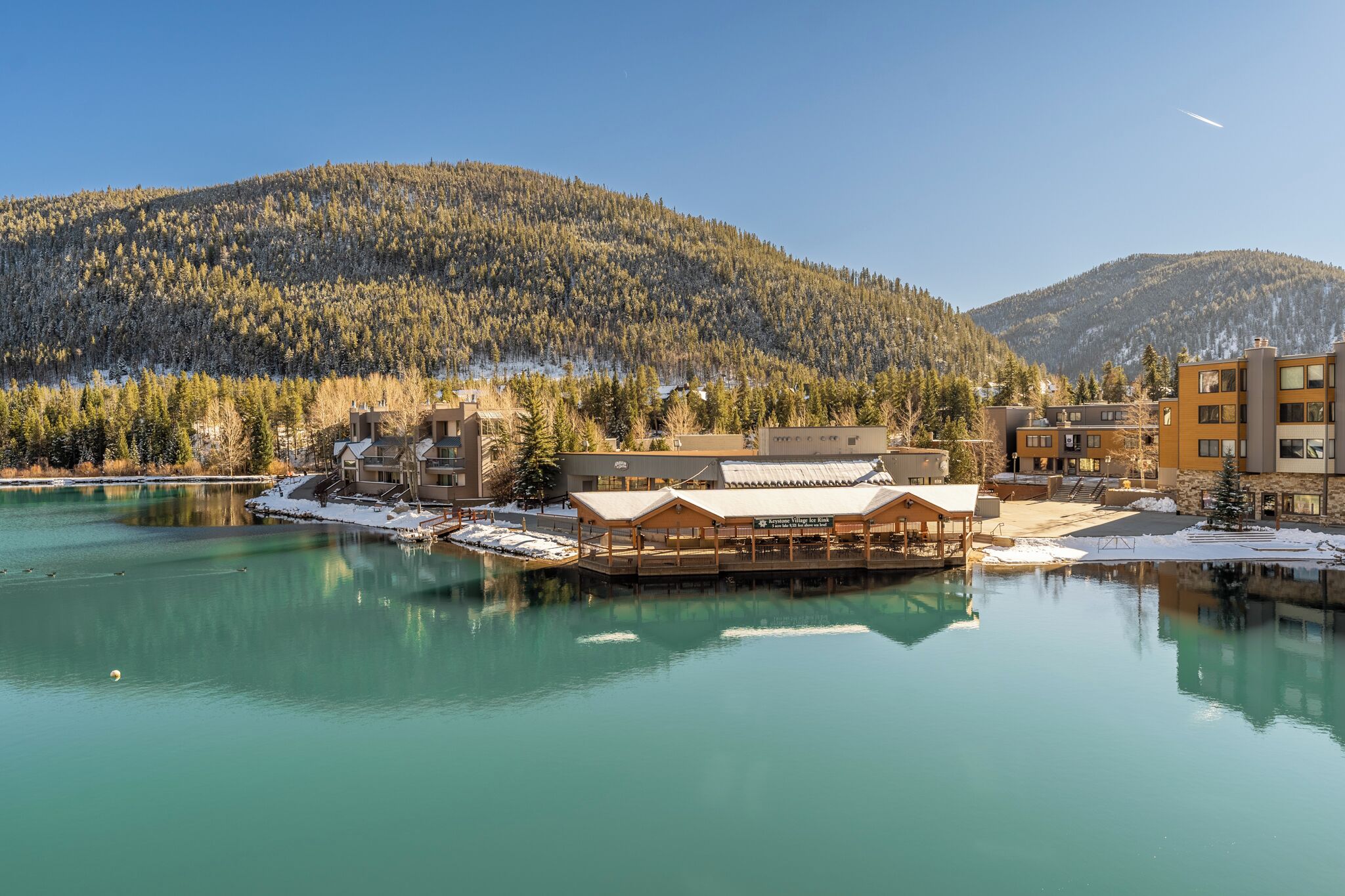Ein Chalet am Seeufer mit einer Holzdar Terrasse und Blick auf einen bewaldeten Berg.