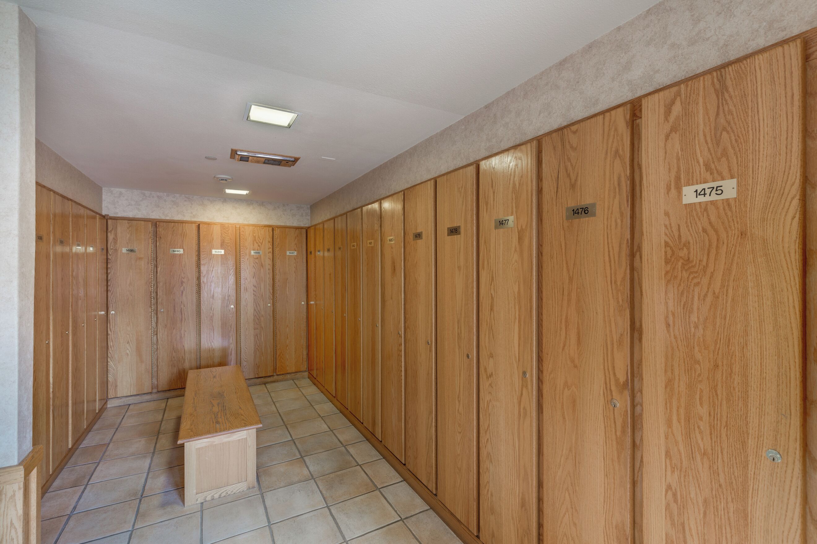 A hallway with wooden lockers numbered 1476 to 1475, a bench, and a tiled floor.