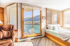 A bedroom with a bed, a chair, and a sliding glass door leading to a balcony with a mountain view.