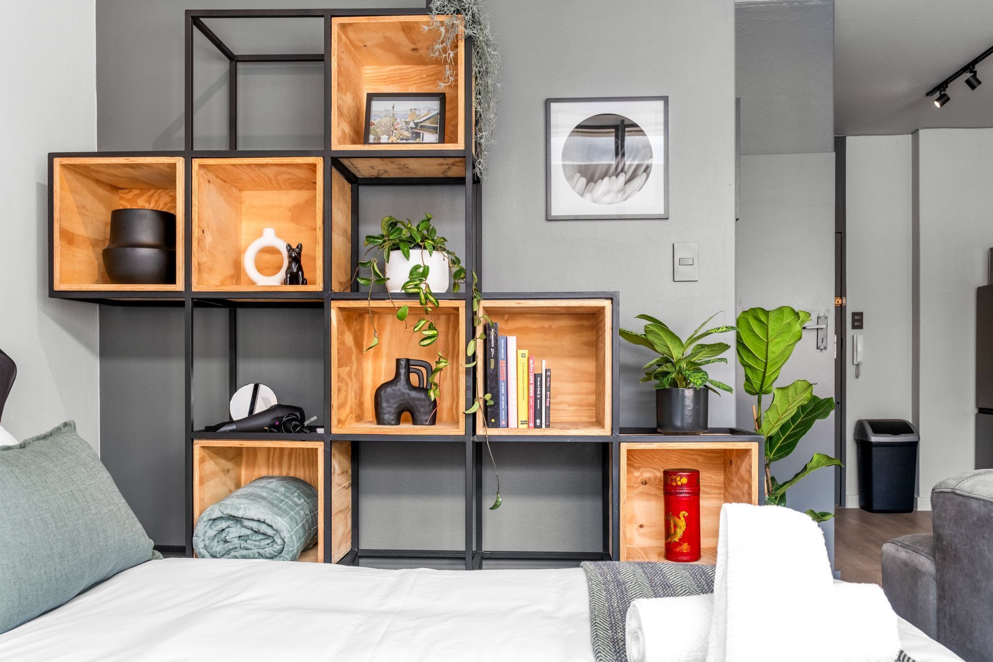 Een moderne kamer met een bed, een grijze bank en een houten boekenkast met diverse spullen.