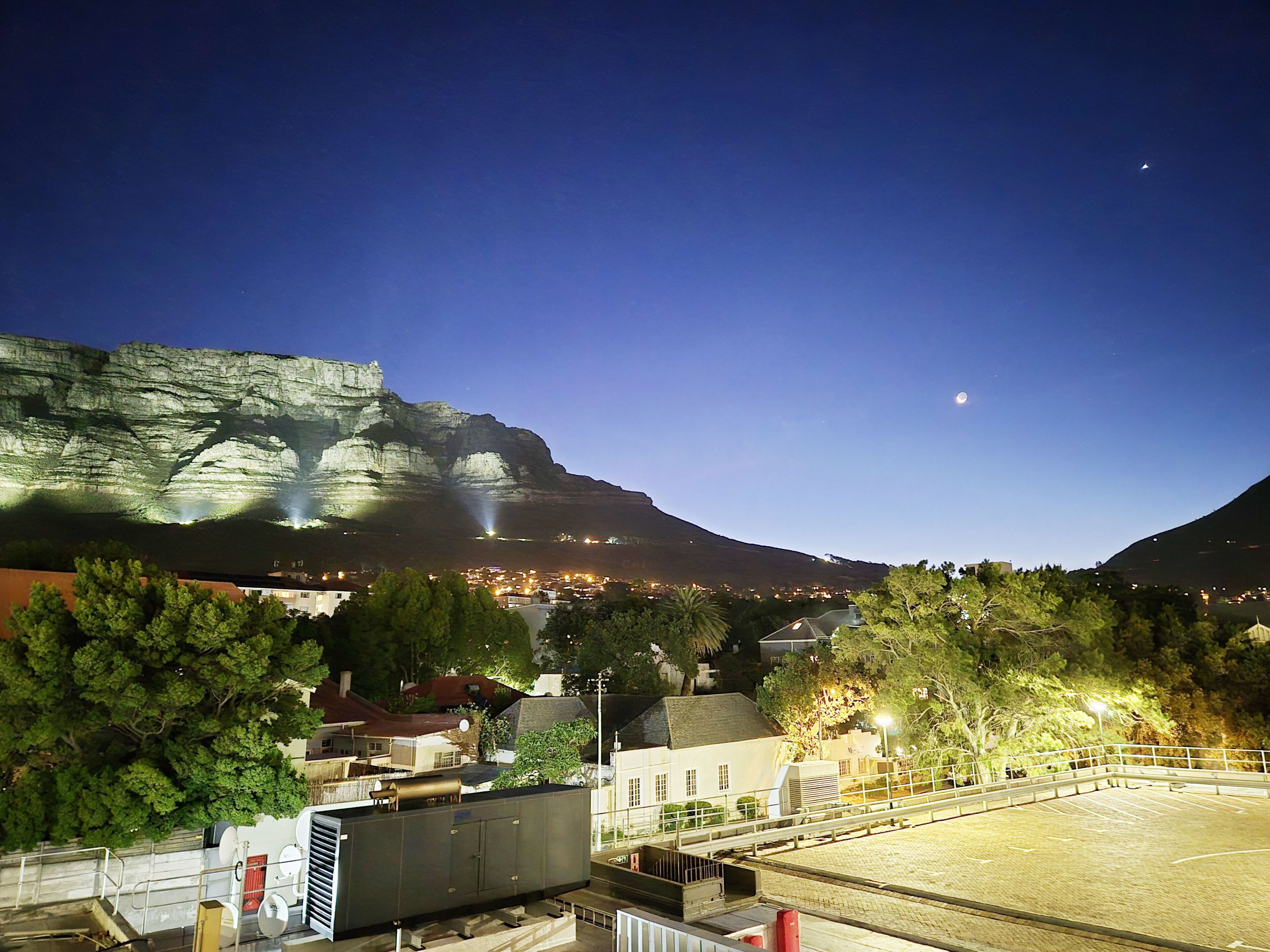 A nighttime view of a town with a prominent cliff and a lit stadium.