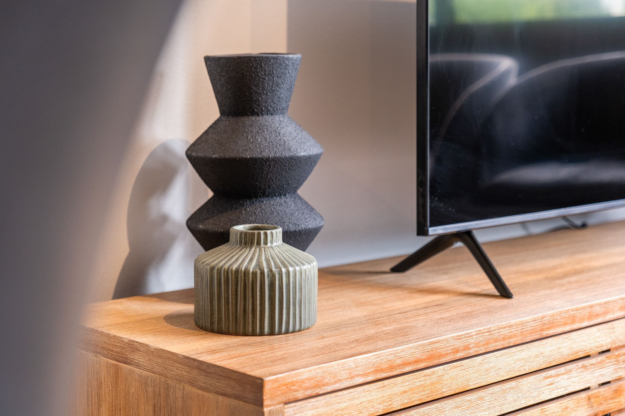 Un tavolo consolle in legno con un vaso decorativo e un televisore su un mobiletto.