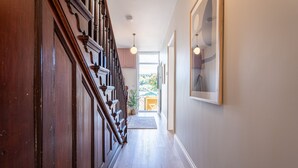 Una escala de fusta que porta a una porta, un quadre amb marc a la paret i una vista d'una casa verda per una porta oberta.