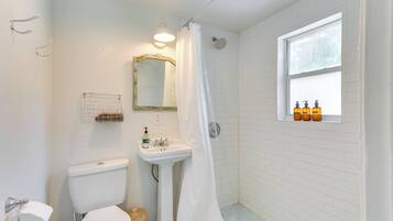 A bathroom with a toilet, sink, shower, and a window with bottles.