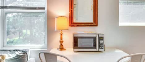 A small dining area with a table, chairs, a lamp, a microwave, and a framed mirror on the wall.