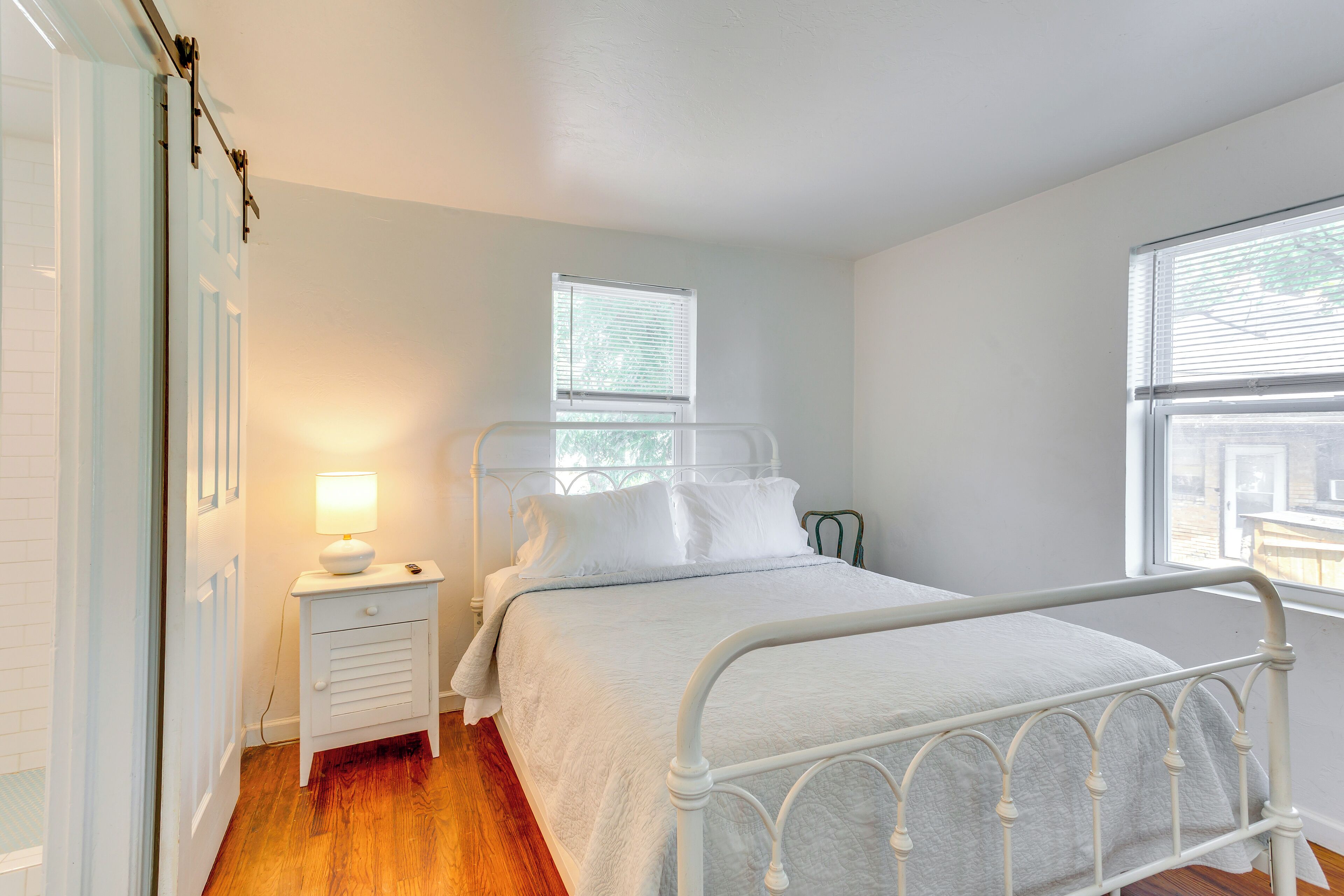 A bedroom with a white metal bed frame, a bedside table with a lamp, and a window with blinds.