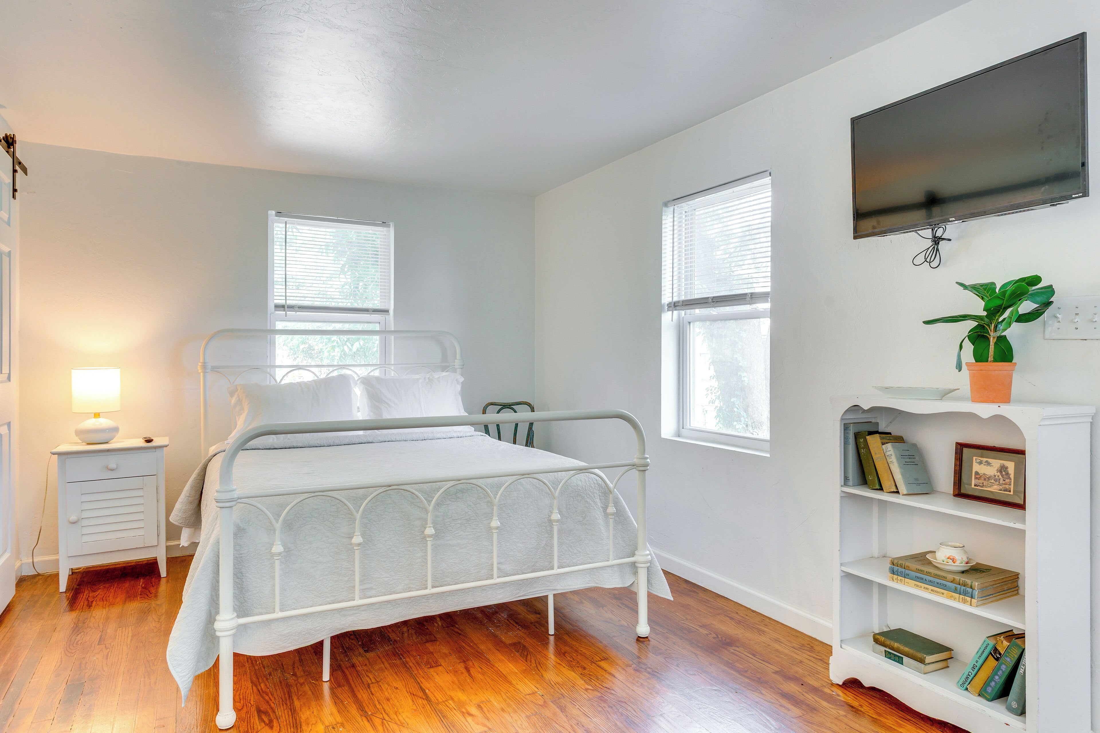 Une chambre à coucher avec un lit en métal, une table de chevet avec une lampe, une bibliothèque et un téléviseur fixé au mur.