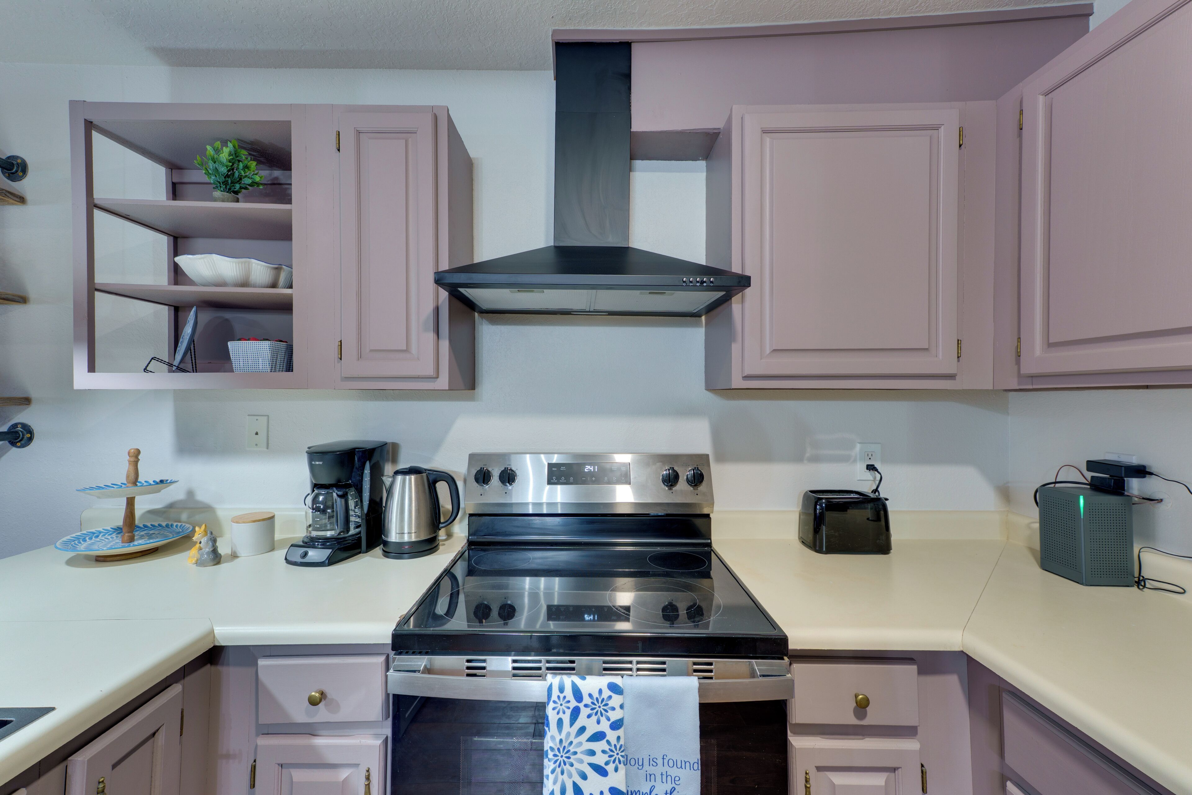 A kitchen with pink cabinets, a stainless steel stove, a coffee maker, and a toaster.