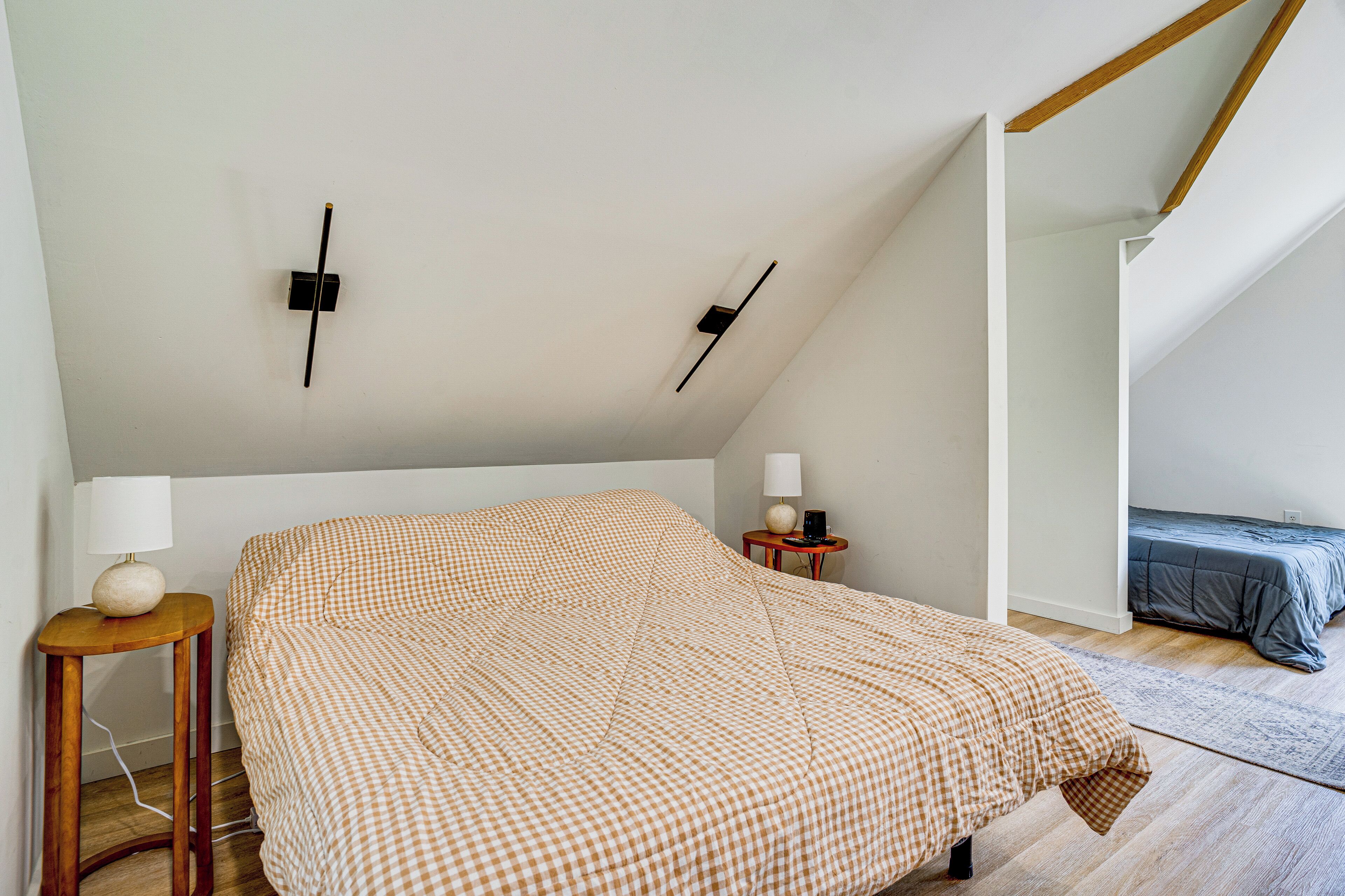 A bedroom with a checkered bedspread, a bedside table with a lamp, and a small bedside table with a lamp and a decorative item.