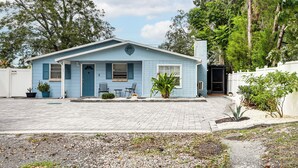 A small, single-story house with a blue exterior, a front porch with two chairs, and a small garden area with plants and a cactus. - Screened Porch: Tampa Studio 4 Mi to Busch Gardens (Tampa)