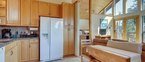 Una cocina con armarios de madera, un refrigerador blanco y una zona de comedor con banco y mesa.