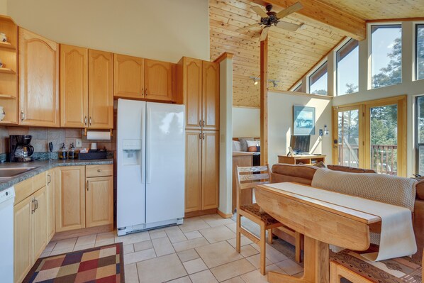 A kitchen with wooden cabinets, a white refrigerator, and a dining area with a bench and table. - Mtn-view Deck: Cabin Getaway in Angel Fire (Angel Fire)