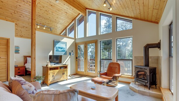 A spacious living room with a high ceiling, large windows, a fireplace, and a cozy seating area. - Mtn-view Deck: Cabin Getaway in Angel Fire (Angel Fire)