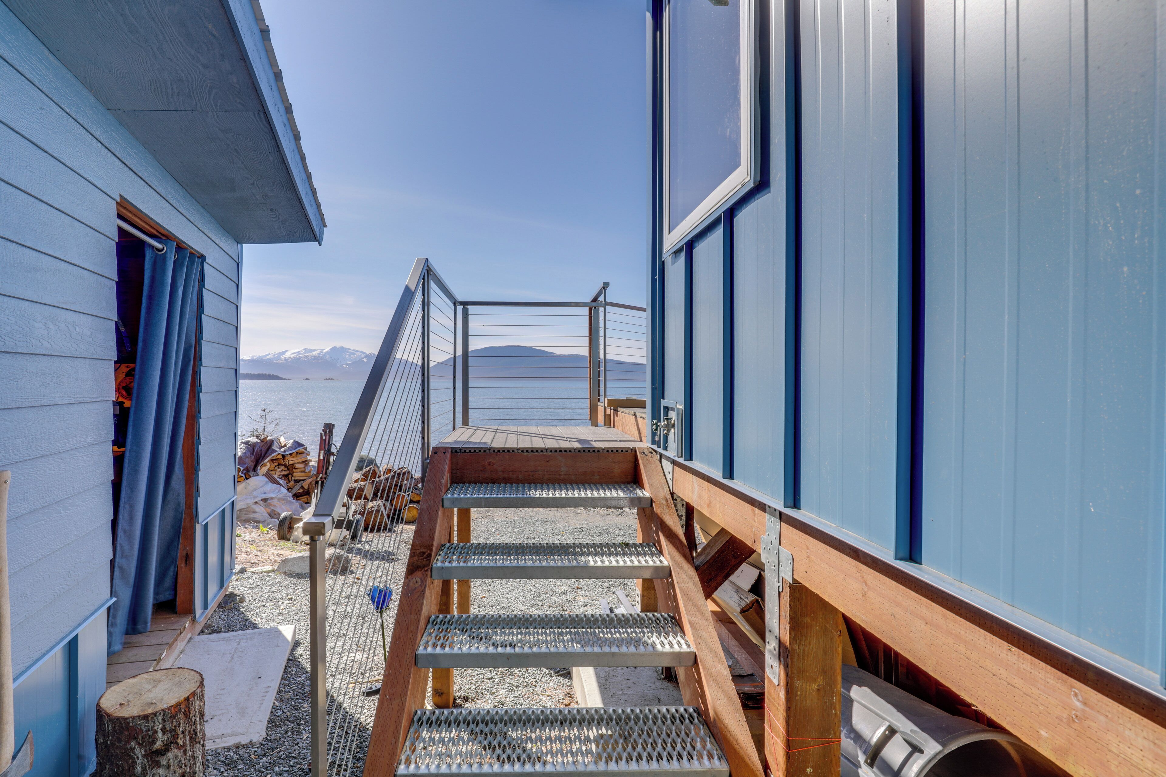 A wooden staircase leading to a deck with a metal railing, overlooking a body of water and mountains.