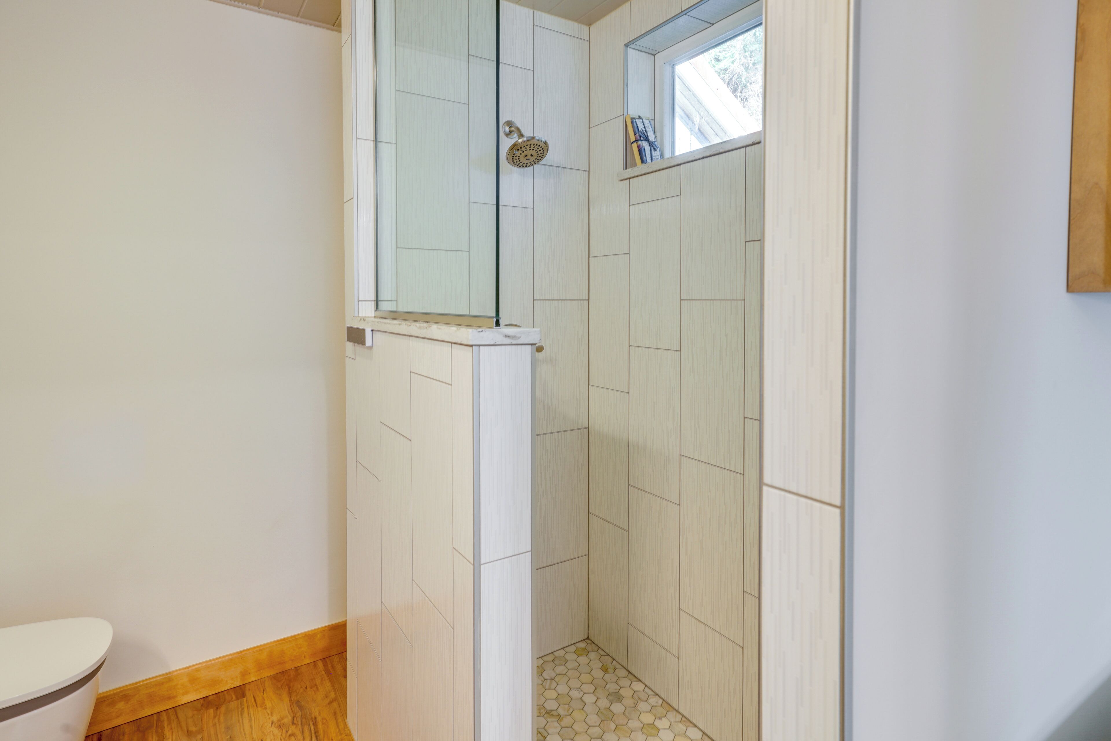 A bathroom with a shower, toilet, and a window.