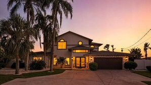 A modern two-story house with a driveway, palm trees, and a sunset sky. - Waterfront Oasis – 6BR Home w/ Pool, Spa & kayaks (Largo)