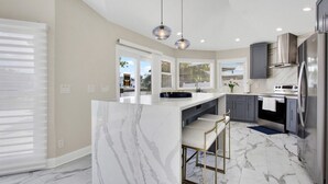 A modern kitchen with a marble island, stainless steel appliances, and pendant lighting. - Waterfront Oasis – 6BR Home w/ Pool, Spa & kayaks (Largo)