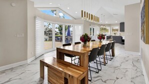 A spacious dining area with a wooden table and chairs, large windows, and a view of the outdoors. - Waterfront Oasis – 6BR Home w/ Pool, Spa & kayaks (Largo)