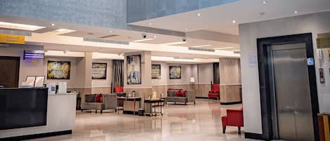 A spacious lobby with a modern chandelier, a reception desk, and a red seating area.