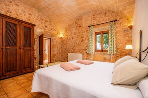 Une chambre aux murs de pierre, avec un lit, une armoire en bois et une fenêtre avec des rideaux.