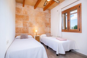Ein Zimmer mit zwei Betten, einer Steinwand, einem Fenster mit Holzrahmen und einem Nachttisch mit Lampe.
