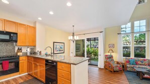 A spacious kitchen with wooden cabinets, a granite countertop, and a dishwasher. There is a dining area with a colorful sofa and a table. - Summer Deal Waikoloa Townhome with Resort Pools Hot Tub and A-Bay (Waikoloa)
