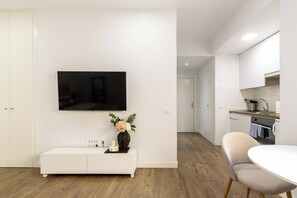 A modern living room with a flat-screen TV, a white console table with candles, and a vase with flowers.