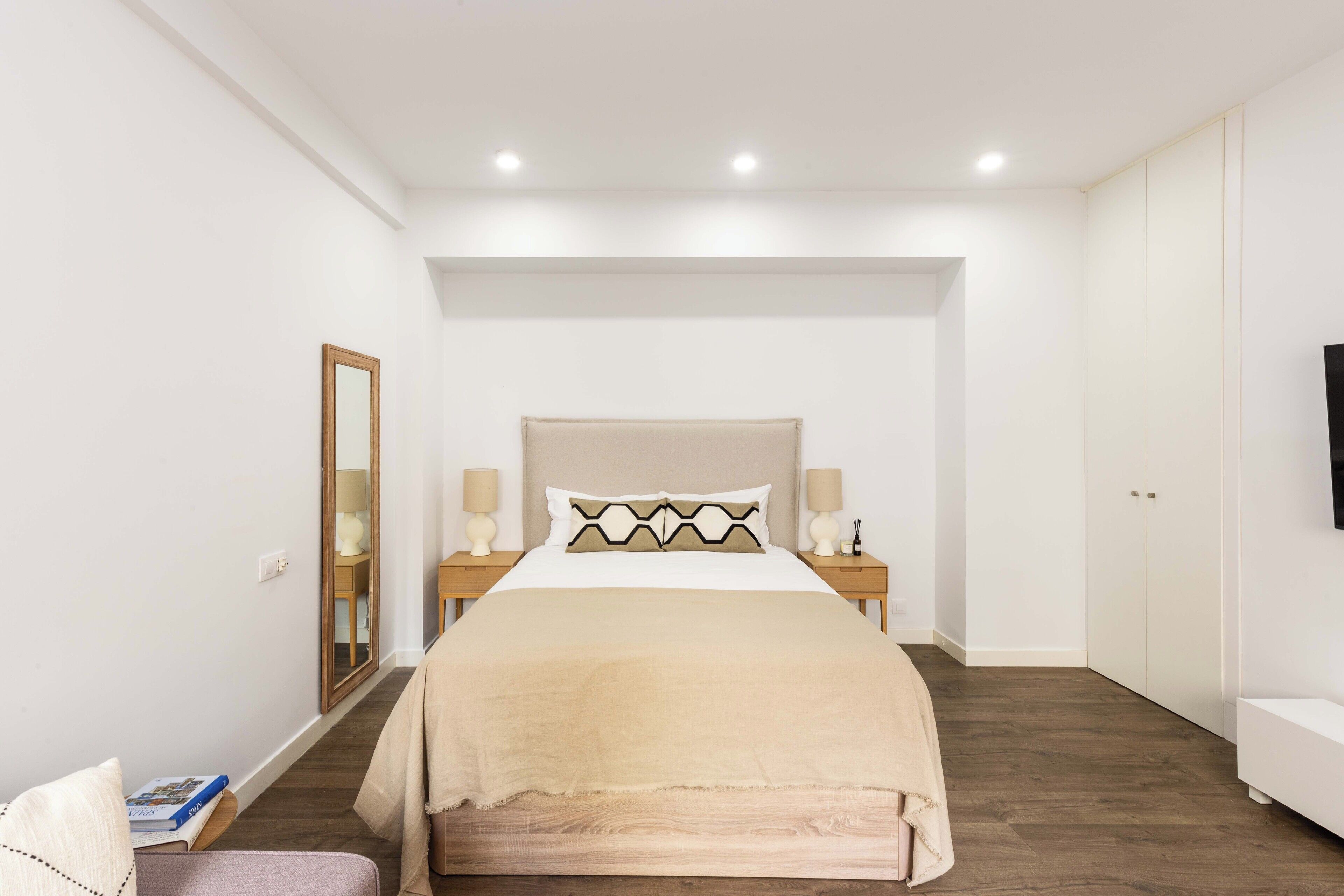 A bedroom with a bed, bedside tables, a mirror, and a TV.