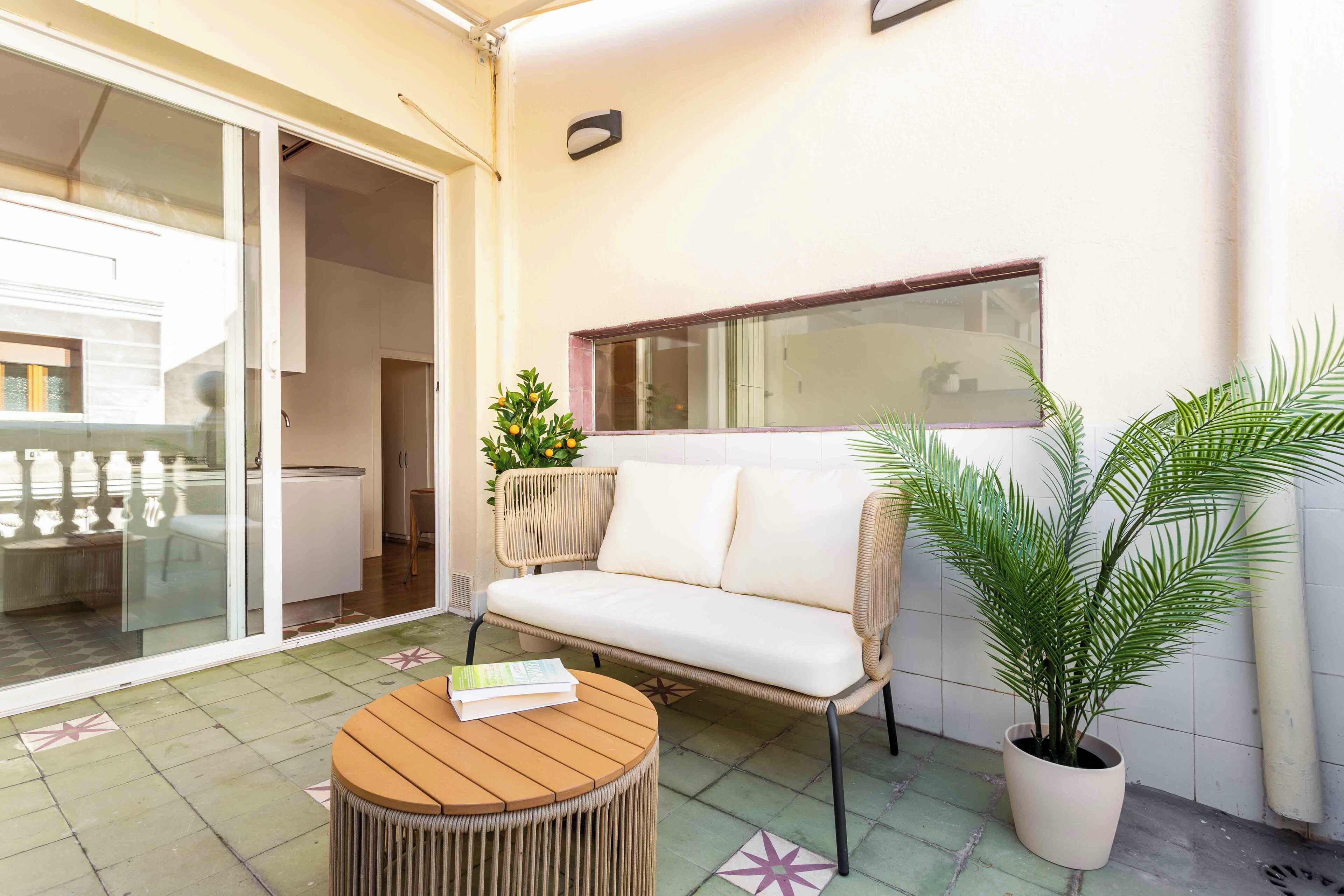 Ein Balkon mit einer Couch, einem Holztisch und Topfpflanzen.