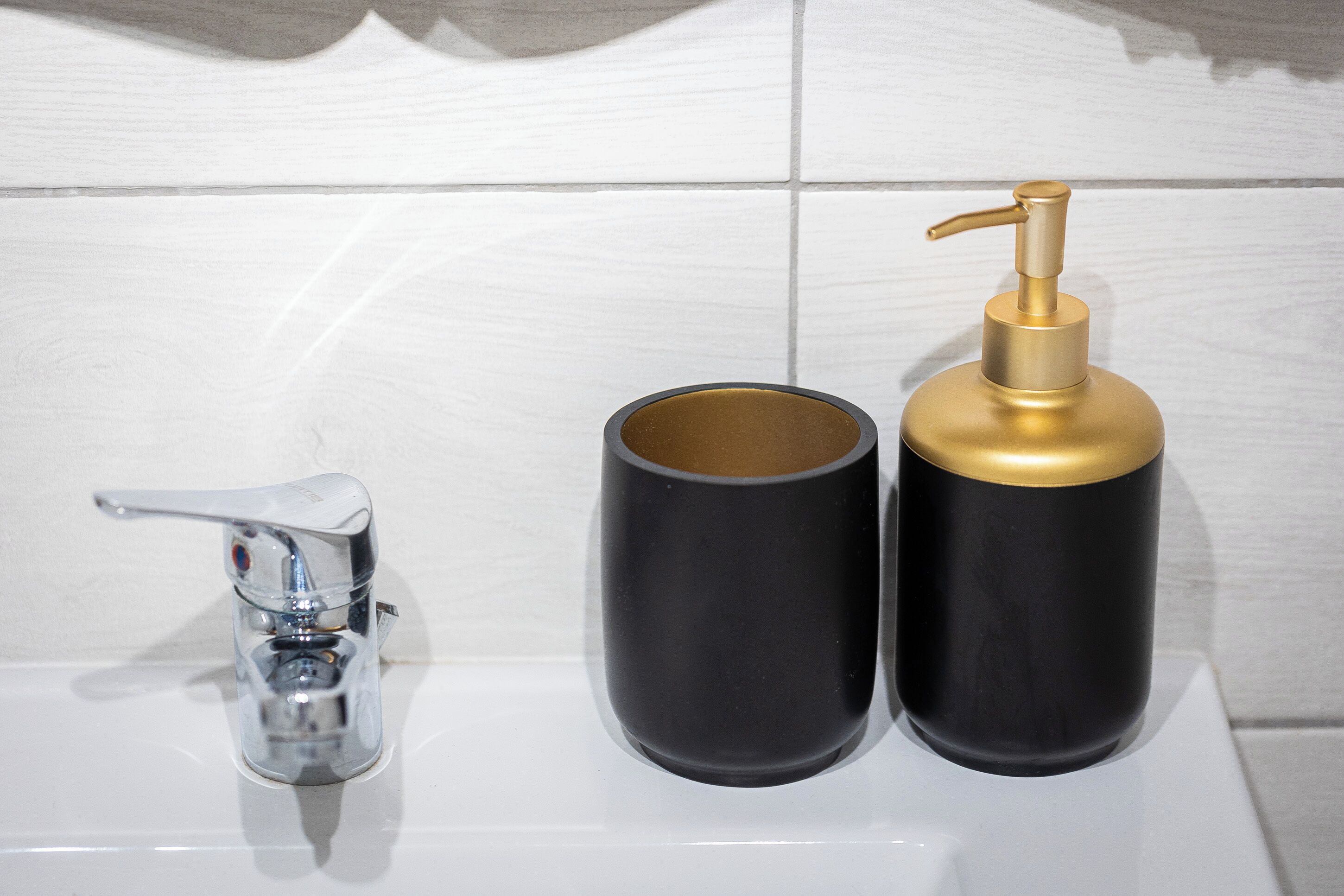 A bathroom with a chrome faucet and two black dispensers, one with a gold pump.