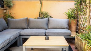 Et moderne udendørs opholdsområde med en grå hjørnesofa, et træbord og forskellige potteplanter.
