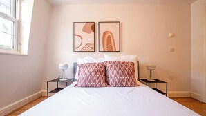 A bedroom with a large bed, two bedside tables, and two wall-mounted lamps. - Kensington & Earls Court 1 bed Apartment - 4 Guest (London)