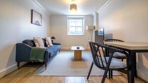 A modern living room with a sofa, a dining table, and a TV. - Kensington & Earls Court 1 bed Apartment - 4 Guest (London)