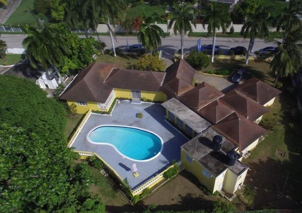 A residential property with a swimming pool, multiple houses, and surrounding greenery.