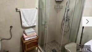 Ein Badezimmer mit einer Duschkabine, einem hölzernen Stuhl mit gefalteten Handtüchern und einer Ablage für Toilettenartikel.