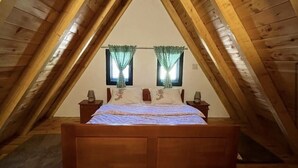 Ein Schlafzimmer mit Holzboden und geneigtem Dach, ausgestattet mit einem Bett, zwei Nachttischen und einem Fenster mit Vorhängen.