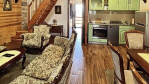 Ein Loft-Zimmer mit einer Holztreppe, einer Couch, einem Esstisch und einer Küchenzeile mit grünen Schränken.
