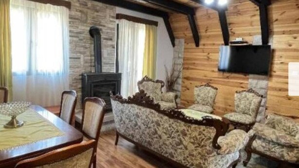 Ein gemütliches Wohnzimmer mit Kamin aus Stein, Holzbalken und gemusterten Sesseln.