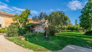 Une maison de campagne, avec une allée en gravier, entourée d’une végétation luxuriante et d’arbres.