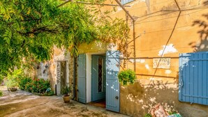 Une cour avec un bâtiment, une porte bleue et une chaise en osier avec des coussins.
