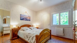 Une chambre avec un lit en bois, une table de chevet avec une lampe, une fenêtre donnant sur un paysage verdoyant et un radiateur.