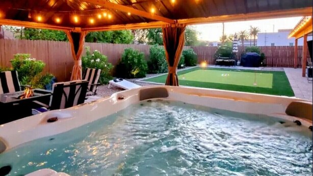 Ein Whirlpool unter einem überdachten Bereich mit Lichterkette, umgeben von Gartenmöbeln und einer Rasenfläche.